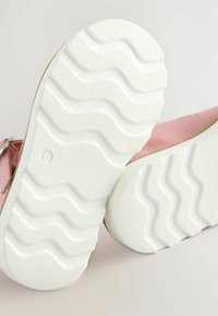 Rosa Schuhe mit einer strukturierten weißen Gummisohle, die wellenförmige Muster aufweist. Weiches Obermaterial, die Unterseite zeigt ein Profil-Design für besseren Halt.