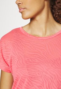 Krótki rękaw, koralowo-różowa koszulka z delikatnym wzorem zebry i okrągłym dekoltem, wykonana z lekkiego, teksturowanego materiału.