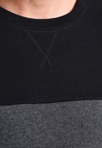Sudadera de cuello redondo en negro y gris con textura acanalada, detalle de costura cruzada en el escote y un diseño a rayas.
