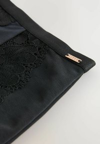 Zwarte stoffen pouch met een textuur van kant, satijnen afwerking en een klein metallisch etiket met de inscriptie "LIPSY." Strakke, matte afwerking over het geheel.