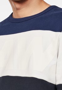 Sudadera de algodón en azul marino y blanco con grandes letras blancas en bloque y cuello redondo acanalado. Detalle de tejido texturizado en la parte inferior.