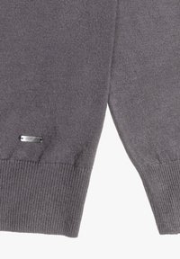 Maglione grigio a maglia con orlo a costine, spacchi laterali e una piccola etichetta metallica sul davanti. Tessuto morbido e di peso medio.