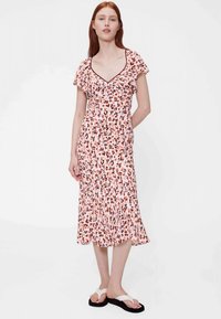 Vidēja garuma kleita ar ziedu rakstu maigi rozā krāsā, ar īsām volānu piedurknēm, piegulošu augšdaļu un platu apakšmalu. Valkāta ar plakanām sandālēm.