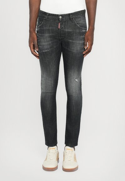 Zwarte spijkerbroek met een slim fit, met subtiele vervaging, versleten details op de knieën en voorzakken. Gecombineerd met lichte sneakers.