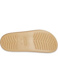 Semelle de chaussure en caoutchouc beige clair avec une texture et un motif antidérapant, comportant le nom de la marque 'crocs' et la taille 'W 7' estampés dans le matériau.