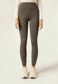 Leggings taille haute, de couleur vert olive foncé, avec un tissu lisse et extensible. Caractéristiques d'un design sans coutures et d'une silhouette ajustée.