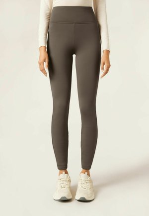 Leggings taille haute, de couleur vert olive foncé, avec un tissu lisse et extensible. Caractéristiques d'un design sans coutures et d'une silhouette ajustée.