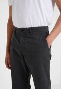 Tmavě šedé bavlněné kalhoty s volným střihem, vybavené zapínáním na knoflíky a bočními kapsami. Hladká textura a minimální šití.