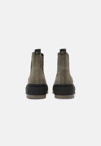 Botas de tobillo de ante verde con suela de goma negra, que cuentan con una pestaña en la parte posterior y un diseño liso y minimalista.