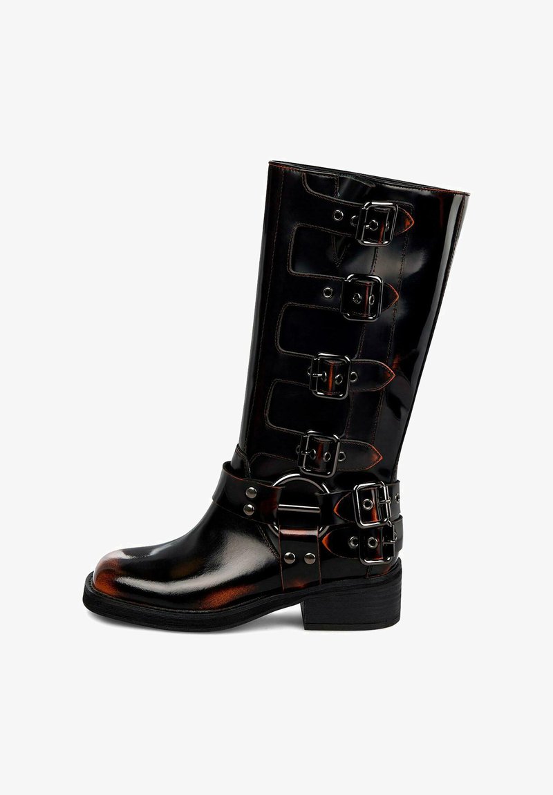 Bota alta de cuero negro brillante con cuatro hebillas laterales y una correa adicional de doble hebilla alrededor del tobillo, sobre un tacón bajo apilado.