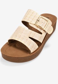 Sandalias blancas con textura de cocodrilo, dos correas anchas, hebilla adjustable y plantilla acolchada marrón sobre una suela tipo corcho en cuña.