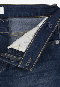 Jeans de mezclilla azul oscuro con cremallera, costuras amarillas en contraste y un forro de bolsillo de tela. Presenta dos botones y un ajuste entallado.