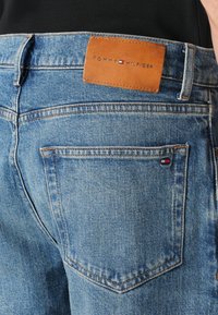 Blauwe denim jeans met een bruine leren patch met het "TOMMY HILFIGER" logo. Klassiek vijf-pocket ontwerp en contrasterende stikseldetails.