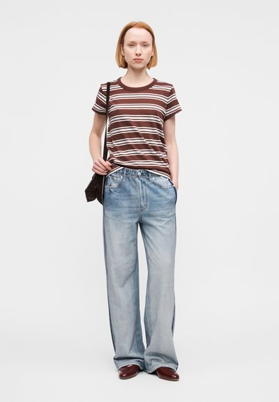 Ριγέ καφέ και λευκό t-shirt σε συνδυασμό με ανοιχτό μπλε τζιν παντελόνι με φαρδιά πόδια. Το σύνολο έχει άνετη εφαρμογή και συνοδεύεται από μια σκούρα τσάντα.