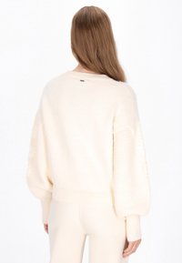 Cremefarvet sweater med ballonærmer, teksturerede strikdetaljer og ribbet kant. Simpelt design med en diskret etiket i nakken.