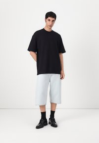 Tricou din bumbac negru, oversized, pantaloni scurți din denim deschis, pantofi negri de dress și șosete negre. Stil simplu, lejer, cu umeri droppați.