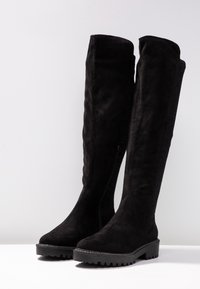 Schwarze, kniehohe Stiefel aus Wildleder mit einem seitlichen Reißverschluss und strukturierten Stoffpaneelen. Verfügen über eine dicke, gerippte Gummisohle für guten Halt.