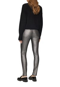 Metaliczne srebrne rurki zestawione z czarnym oversize'owym swetrem i błyszczącymi czarnymi butami, ukazując smukłą, dopasowaną sylwetkę.