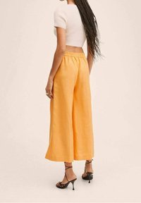 Przycięty biały sweter i pomarańczowe szerokie spodnie z elastycznym paskiem, w połączeniu z czarnymi sandałami na obcasie. Gładka tekstura, luźny krój.