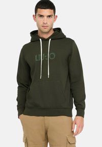 Donkergroene hoodie met een voorzak, verstelbare witte trekkoorden en een licht vervaagde logografiek. Zachte stoftextuur.