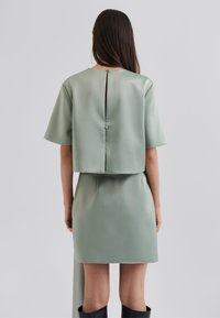Completo in satin verde con un top corto a maniche corte, chiusura posteriore con bottoni e una gonna attillata con una silhouette elegante.