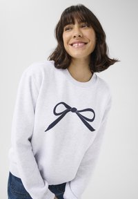 Lichtgrijze sweatshirt met een donkerblauwe strikafbeelding in het midden. Zachte stof met geribde manchetten en zoom, relaxte pasvorm.