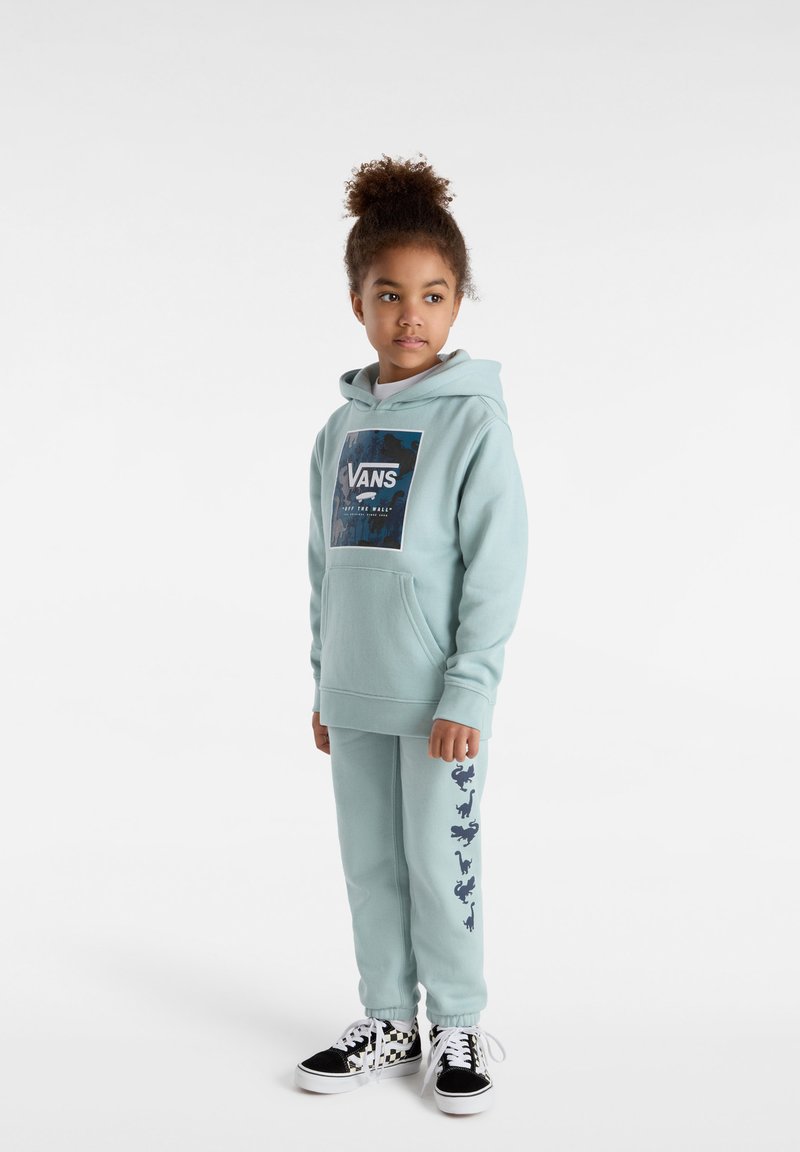 Ljusblå hoodie med Vans-logotyp, framfickor; matchande byxor med marinblå dinosaurmönster, parat med svart-vita rutiga sneakers.
