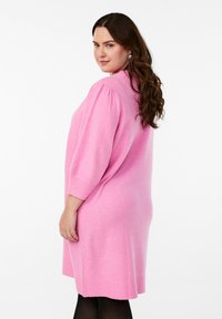 Abito lavorato a maglia oversize rosa con maniche corte a palloncino, polsini e orlo a costine. Texture morbida, vestibilità rilassata e design lungo fino al ginocchio.