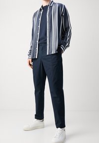 Marinblå och vit randig skjorta med knappar, i kombination med marinblå byxor och vita sneakers. Texturerad tyg med en avslappnad passform.