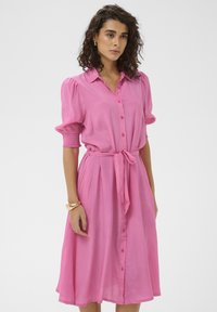Robe courte rose à manches courtes, boutonnée sur le devant, avec une ceinture à la taille et des manches froncées. Tissu léger avec une texture lisse.