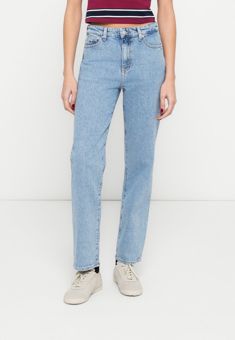 Hele sinised sirge lõikega teksapüksid, valmistatud denimist, millel on kõrge vöökoht, viis taskut ja pehme pleekinud efekt. Kandmas beeže jalanõusid.