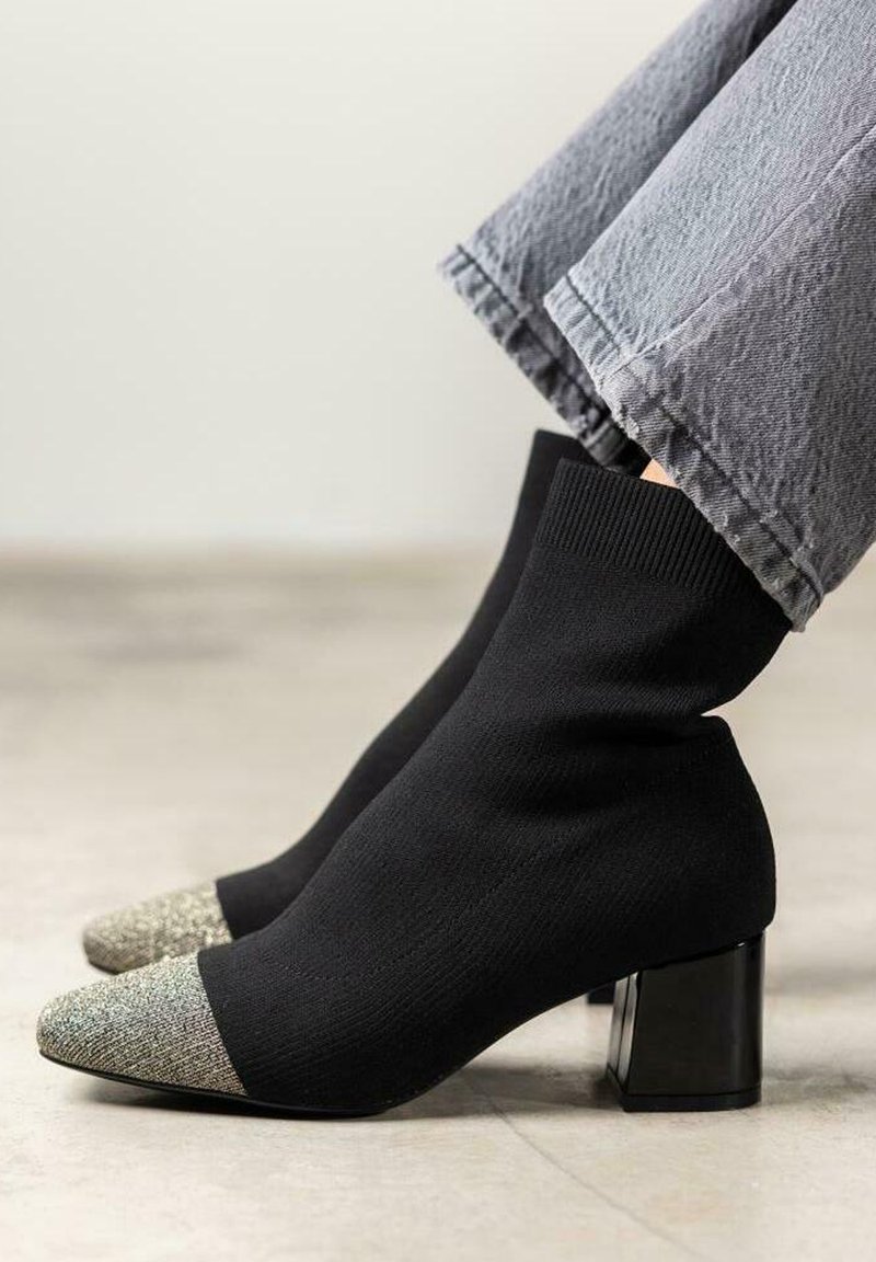 Botas de tobillo estilo calcetín negras con una puntera texturizada y brillante, con un tacón grueso negro y un ajuste ceñido alrededor del tobillo.