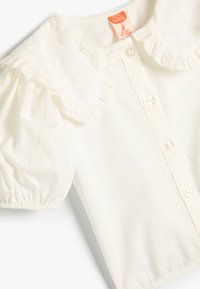 Weiße, knöpfbare Bluse für Babys mit einem gerafften Kragen und besticktem Blumenmuster. Puffärmel und weicher, leichter Stoff.