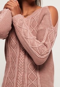 Großer Rippstrickpullover in sanftem Pink. Mit offenem Schulterdesign, aufwendigen Strickmustern und gerippten Bündchen. Aus Baumwollmischung.