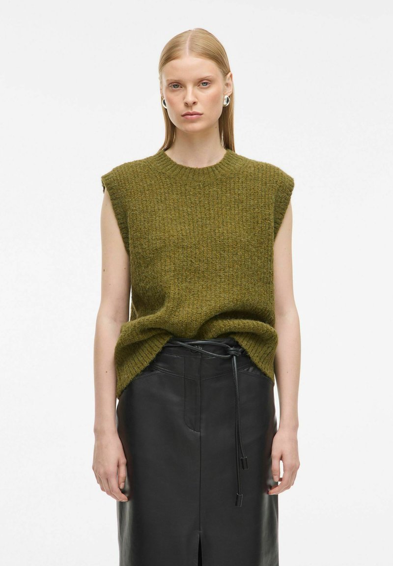 Olivno zelena brezrokavna pletena majica s teksturiranim vzorcem, v kombinaciji z oprijetim črnim usnjenim krilom z razporkom spredaj in podrobnostmi na vrvici.