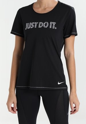 Femme portant un t-shirt noir Nike avec le texte « JUST DO IT. » et des leggings noirs avec des panneaux en mesh et des logos Nike.