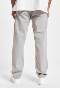 Pantalones anchos de color gris claro hechos de algodón, con una textura suave, bolsillos traseros y pequeños detalles de costura. Combinados con zapatillas blancas.