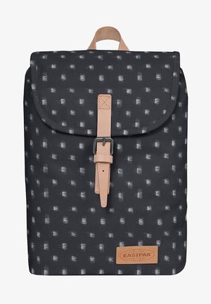 Reppu, jossa on teksturoitu musta kangas, jossa on valkoinen graafinen kuvio, nahkainen olkahihna ja solki, sekä vaalea logo-tarra.