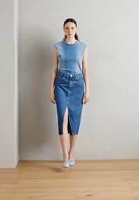 Modrá rebrovaná top bez rukávov v kombinácii s džínsovou ceruzkovou sukňou s predným rozparkom. Model nosí svetlomodré baleríny na drevenej podlahe.