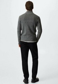 Grauer Strickpullover mit hohem Kragen, kombiniert mit schwarzen Hosen und schwarzen Schuhen. Die Textur wirkt weich und gemütlich.