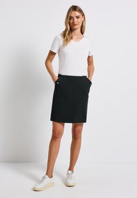 Jupe noire en A avec deux poches avant et des accents de boutons, associée à un t-shirt blanc à col en V et des baskets blanches. Texture de tissu lisse.