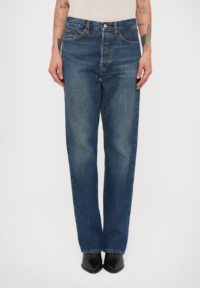 Σκούρα μπλε τζιν με ίσια γραμμή στο πόδι, μεσαία απόχρωση, σχέδιο με πέντε τσέπες και κλείσιμο με κουμπιά μπροστά. Συνδυασμένα με μαύρα μποτάκια με μυτερή μύτη.