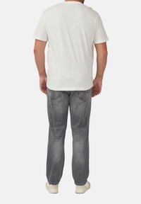 Weißes Baumwoll-T-Shirt mit kurzen Ärmeln, kombiniert mit grauen Jeans aus Denim mit verblasstem Finish und klassischen Gesäßtaschen.