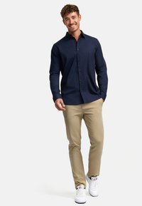 Camisa de botones de manga larga en azul marino, combinada con pantalones caqui y zapatillas blancas. Presenta un cuello clásico y un diseño ajustado.