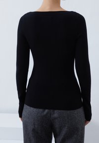 Haut noir ajusté à manches longues avec un large décolleté, une texture côtelée lisse et une silhouette fuselée, associé à un pantalon gris sur mesure.