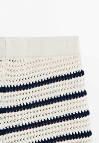 Gros plan sur un tissu tricoté blanc avec des rayures horizontales bleu marine et une ceinture côtelée.