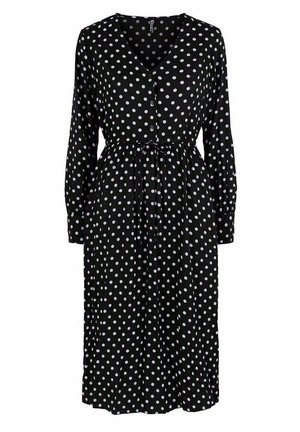 Schwarzes Kleid mit weißen Punkte, langen Ärmeln, V-Ausschnitt, Knopffront, Kordelzugbund und fließendem Rock. Es hat überall weiße Punkte.