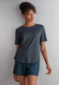 Šedé tričko s krátkým rukávem a kulatým výstřihem, volný střih a měkká textura. V kombinaci s tmavě modrými šortkami, minimalistický design a žádné viditelné vzory.