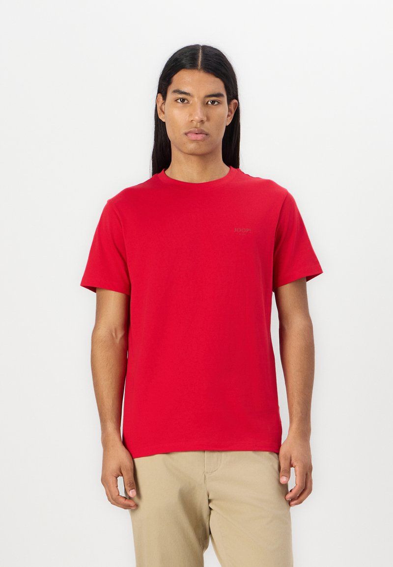 Camiseta de algodón roja con un cuello redondo clásico, mangas cortas y un logotipo sutil en un tono más oscuro en el pecho. Textura suave.