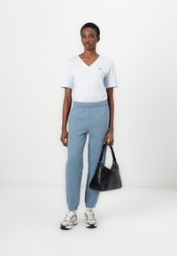 Blå V-hals T-skjorte, lys blå joggebukser, og svart håndveske. Sko med sølvfinish. Minimalistisk, uformelt antrekk med et rent design.